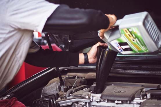 Man with gray shirt pouring oil in a car